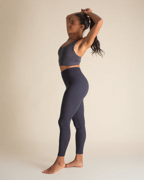 Woman standing stretching hands over her head in a Merino wool compression legging and bra set. BRANWYN's night sky blue leggings are BPAs, PFAs, and forever chemical free.
