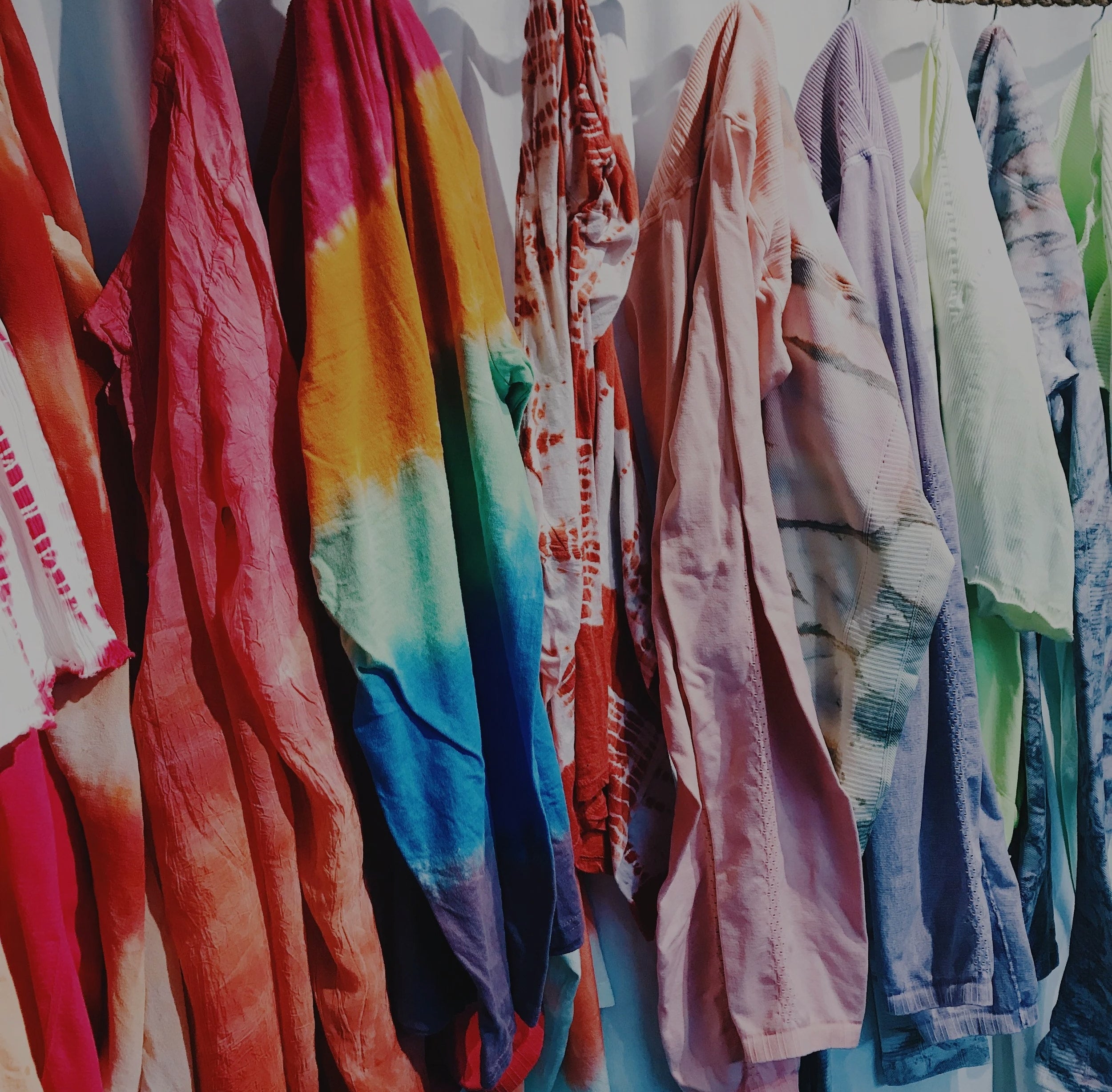 Colorful tie-dye shirts hanging on a line against a white curtain.