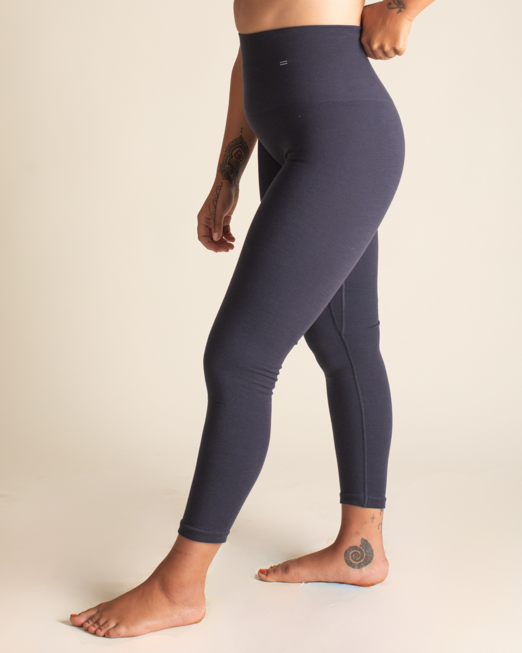 Person wearing dark blue leggings and a light gray sports bra on a beige background