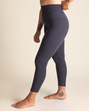 Person wearing dark blue leggings and a light gray sports bra on a beige background
