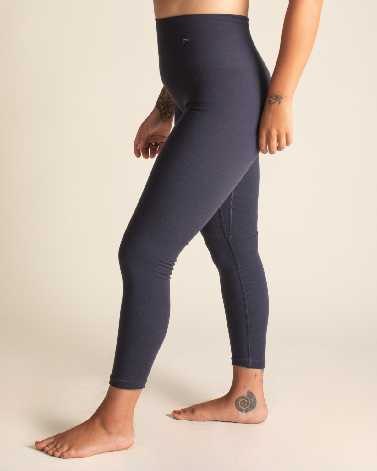 Person wearing navy leggings and a light gray sports bra on a beige background