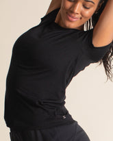 Woman stretching in black Merino wool short sleeve tee, a thermal base layer for hiking, camping, and outdoor adventures.