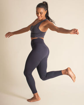 Woman jumping in BRANWYN's Essential Compressive leggings in Night Sky blue. Merino leggings for yoga, gym sessions, or as a warm base layer in for winter.