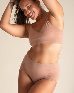 Woman smiling and posing in warm nude Merino underwear set by BRANWYN. Wearing the high waisted Merino Wool Essential Boyshort underwear by BRANWYN.