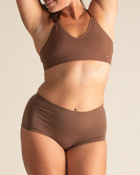 Woman stretching in dark nude Merino wool underwear set by BRANWYN. Wearing the women's Essential Boyshort underwear made of seamless Merino wool natural fibers.