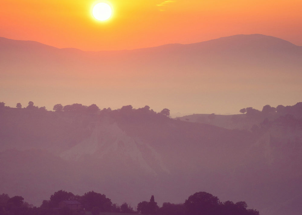 Sunset over a hilly landscape with a visible horizon line.