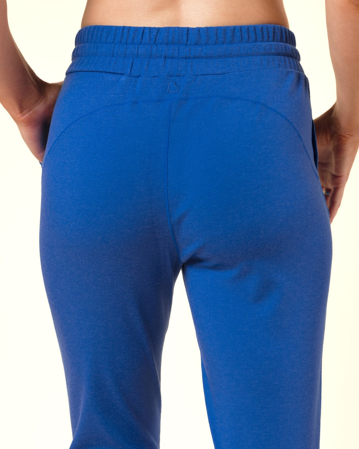 A person shown from the back wearing bright blue sweatpants and a matching blue sports bra against a plain light beige studio background.