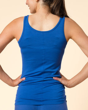A woman with her hair in a ponytail, seen from behind, wearing a bright blue athletic tank top and matching blue leggings against a solid beige background.